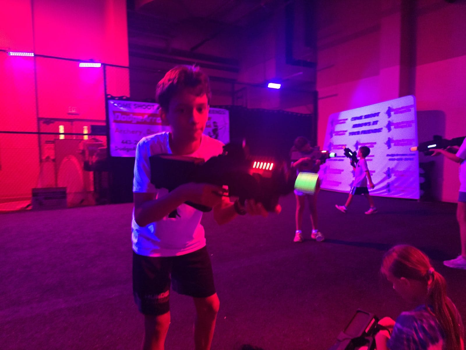 Wide shot of a laser tag game running in the dark arena under pink and purple lighting
